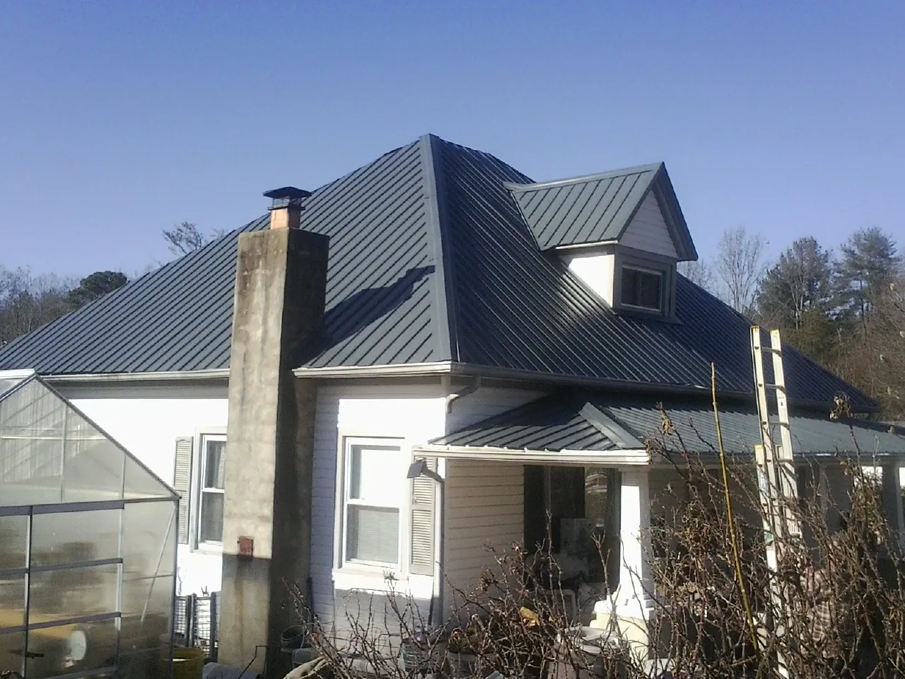 Dark blue standing seam metal roof on a white farmhouse with dormer — Slate & Tile Roof Repair by Roofing Brothers in Unionville