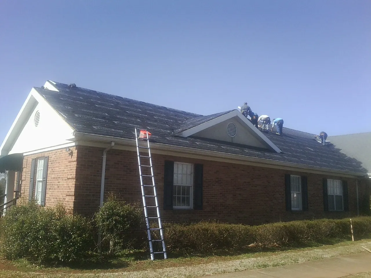 Crew tearing shingles off a brick ranch roof with a ladder set — Emergency Roof Repair work by our crew in Unionville